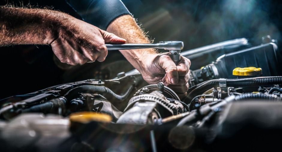 Un hombre está trabajando en el motor de un automóvil con una llave inglesa.