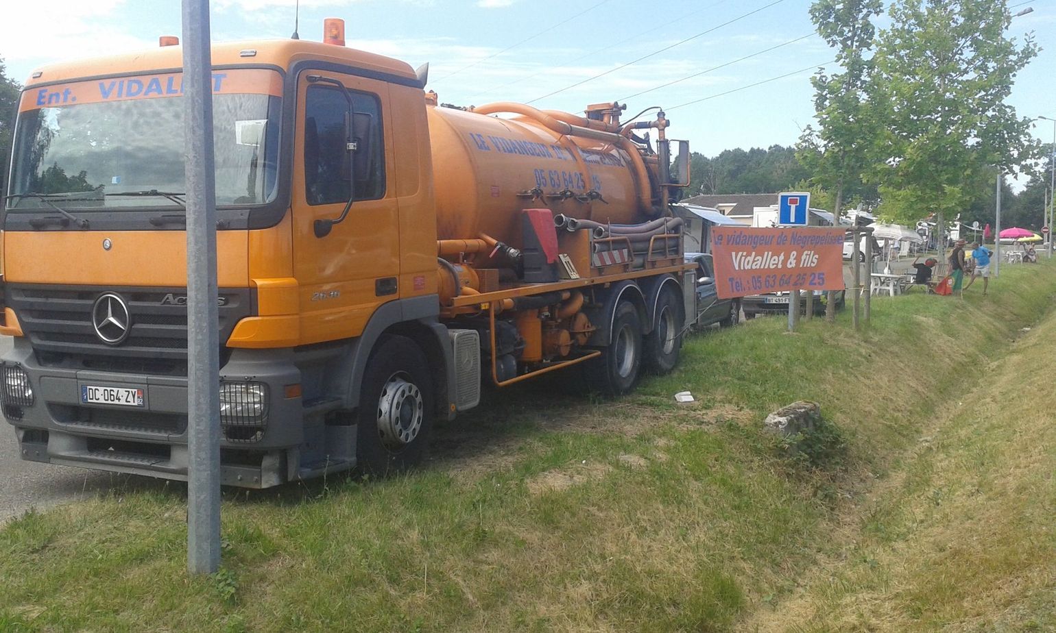Un camion-citerne orange proche d'un terrain herbeux.