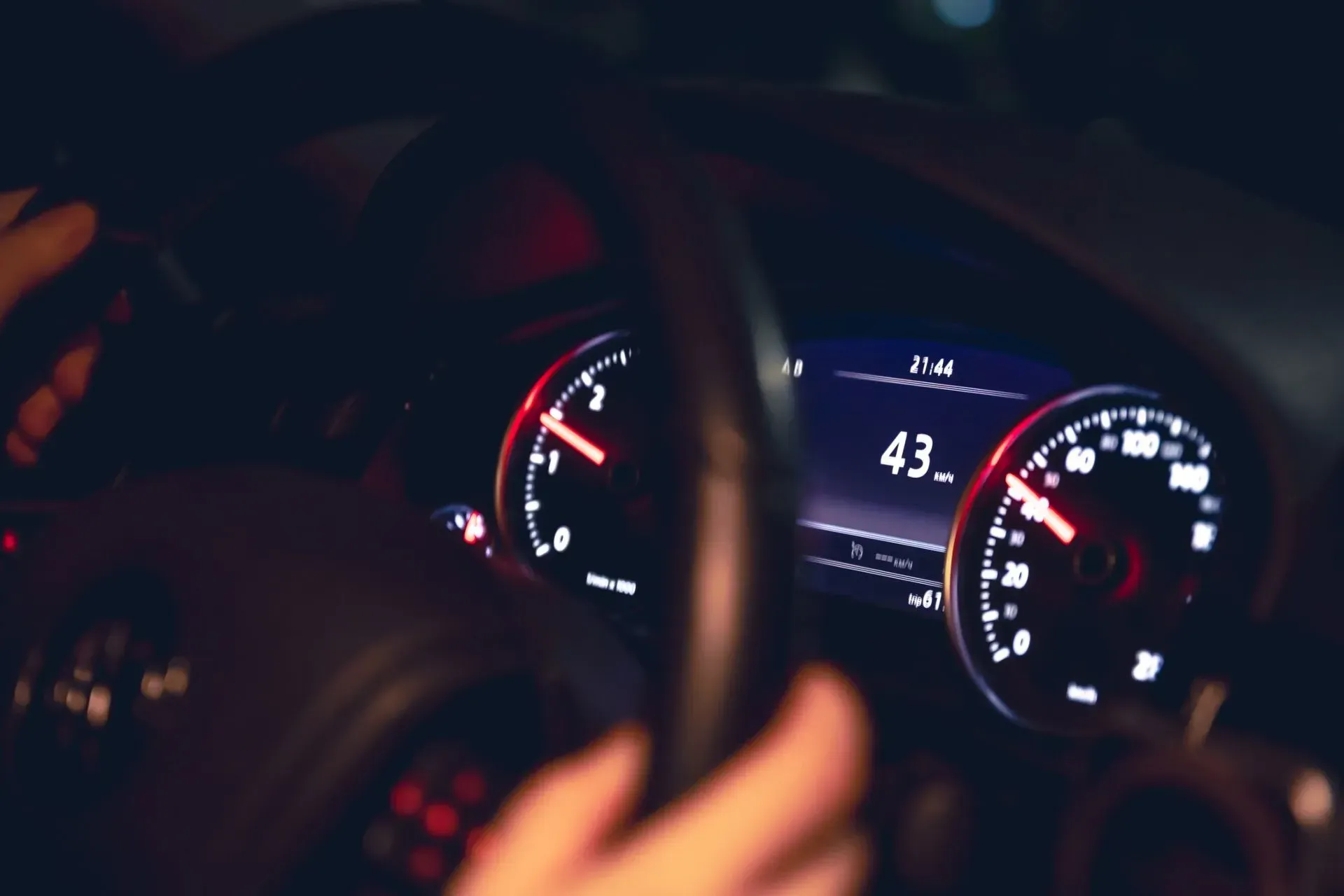 Tablero de un auto por la noche con velocímetro, tacómetro y pantalla digital iluminados que muestran 43 mph.