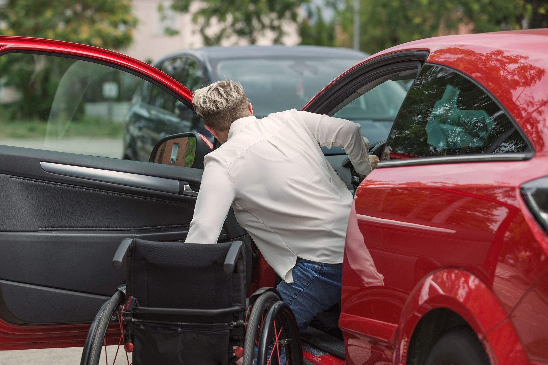 Un hombre en silla de ruedas sale de un coche rojo.