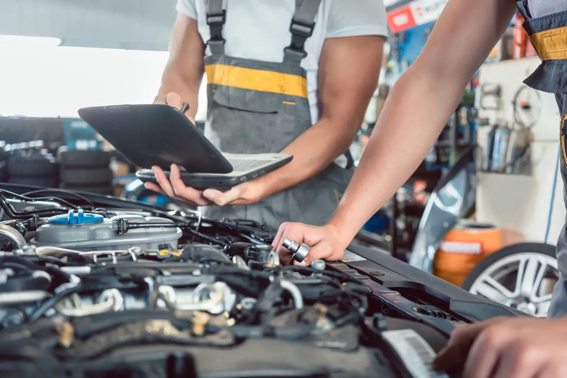Un equipo de mecánicos inspecciona el motor de un coche abierto con un ordenador portátil en un taller de reparación de automóviles.