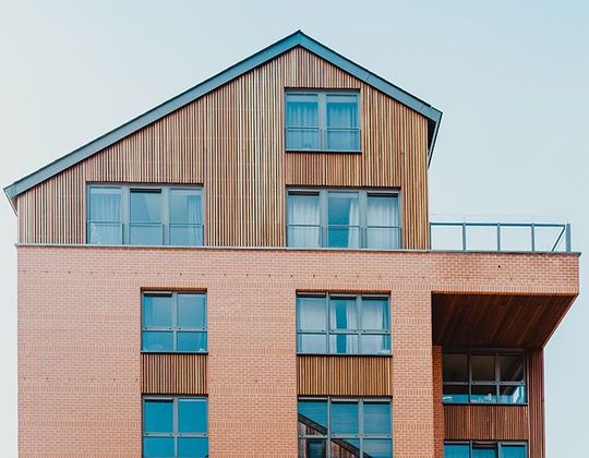 Immeuble moderne à plusieurs étages avec bardage en bois, fenêtres bleues et terrasse sur le toit