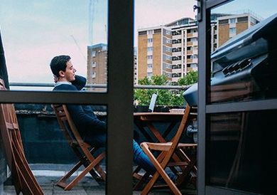 Un homme assis sur une chaise de balcon regarde les immeubles d'appartements de l'autre côté d'une cour.