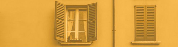Mur jaune avec deux fenêtres à volets, dont une ouverte avec des rideaux, et une rambarde de balcon en dessous.
