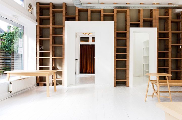 Studio minimaliste lumineux avec murs blancs, grandes fenêtres et hautes étagères en bois autour d'une porte