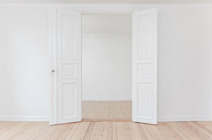 Ouvrez des portes doubles blanches dans une pièce lumineuse et vide, avec un parquet clair.