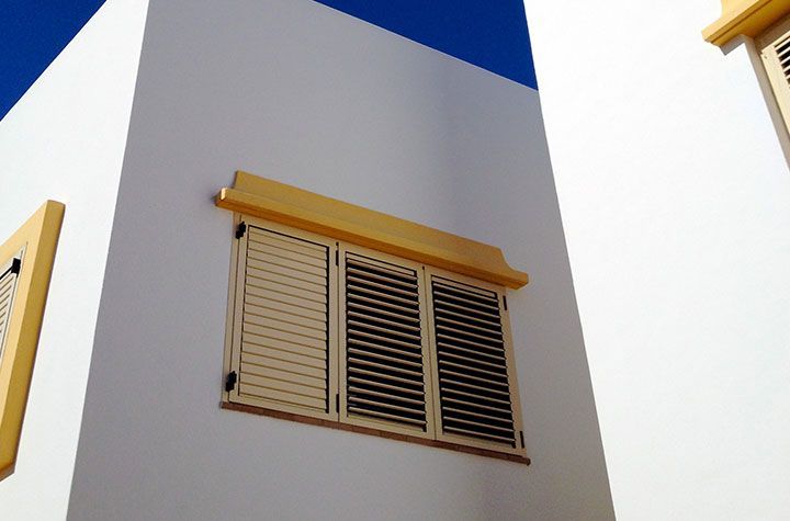 Façade d'immeuble blanche avec fenêtre à volets à bordure jaune se détachant sur un ciel bleu