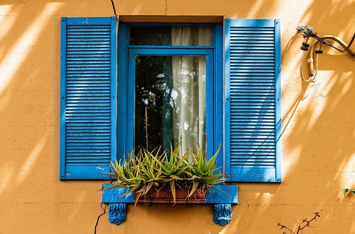 Volets bleus et jardinière sur un mur en stuc jaune autour d'une fenêtre