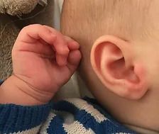 Un primer plano de la oreja y la mano de un bebé.