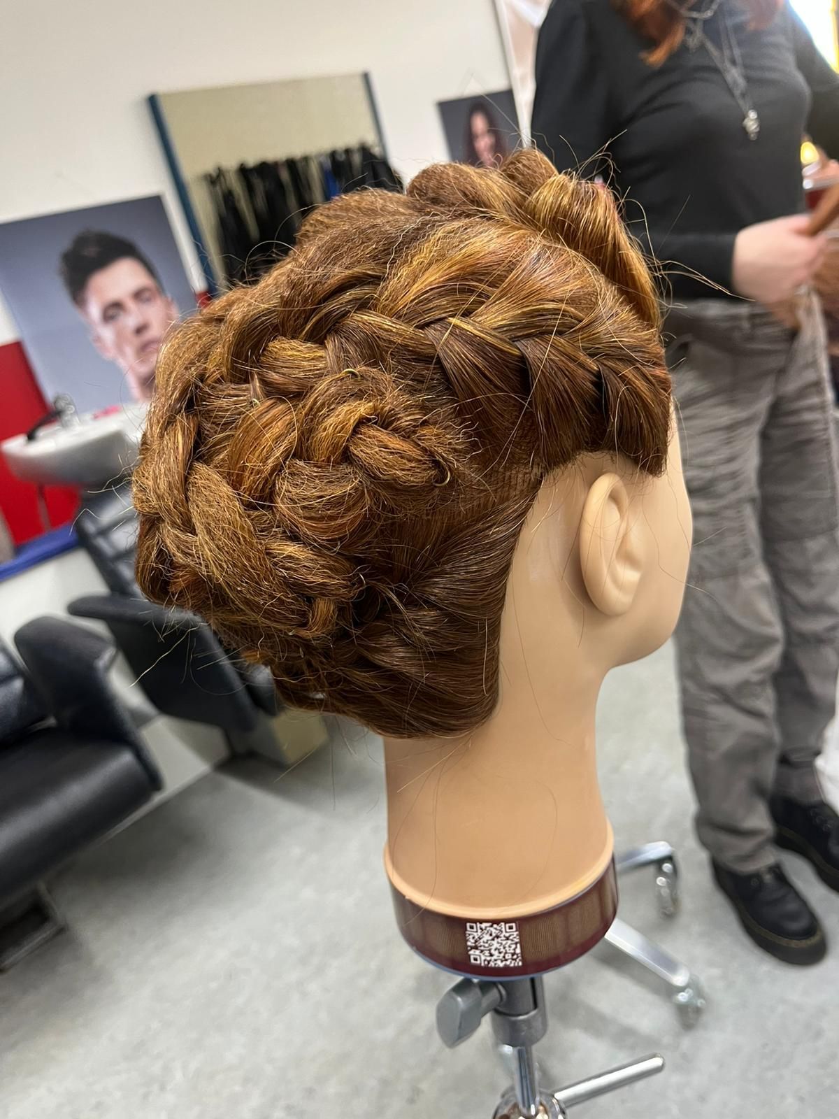 Eine Person, von hinten gesehen, mit langem, gewelltem, hellblondem, gestuftem Haar vor einem blauen Vorhang.