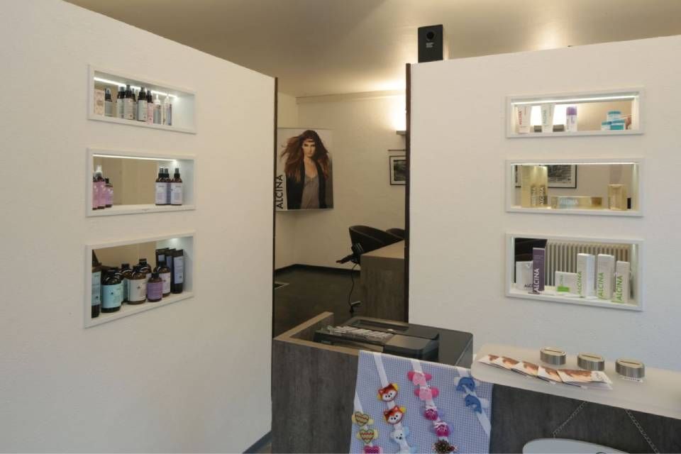 Zwei weiße Wände mit eingelassenen Regalen, die mit Salonprodukten gefüllt sind, flankieren den zentralen Blick auf ein modernes Saloninterieur.