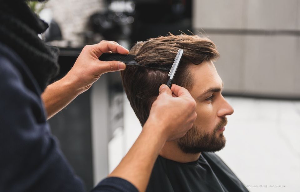 Ein Friseur schneidet einem Mann in einem Salon mit Schere und Kamm die Haare.