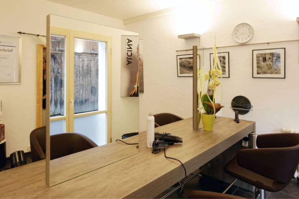 Ein moderner Friseursalon-Arbeitsplatz mit zwei gegenüberliegenden Spiegeln, Holztischen, braunen Stühlen und einer kleinen Topfpflanze.