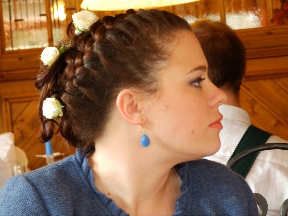 Seitenansicht einer Person mit geflochtener Frisur, die mit drei weißen Blüten verziert ist und einen blauen tropfenförmigen Ohrring trägt.