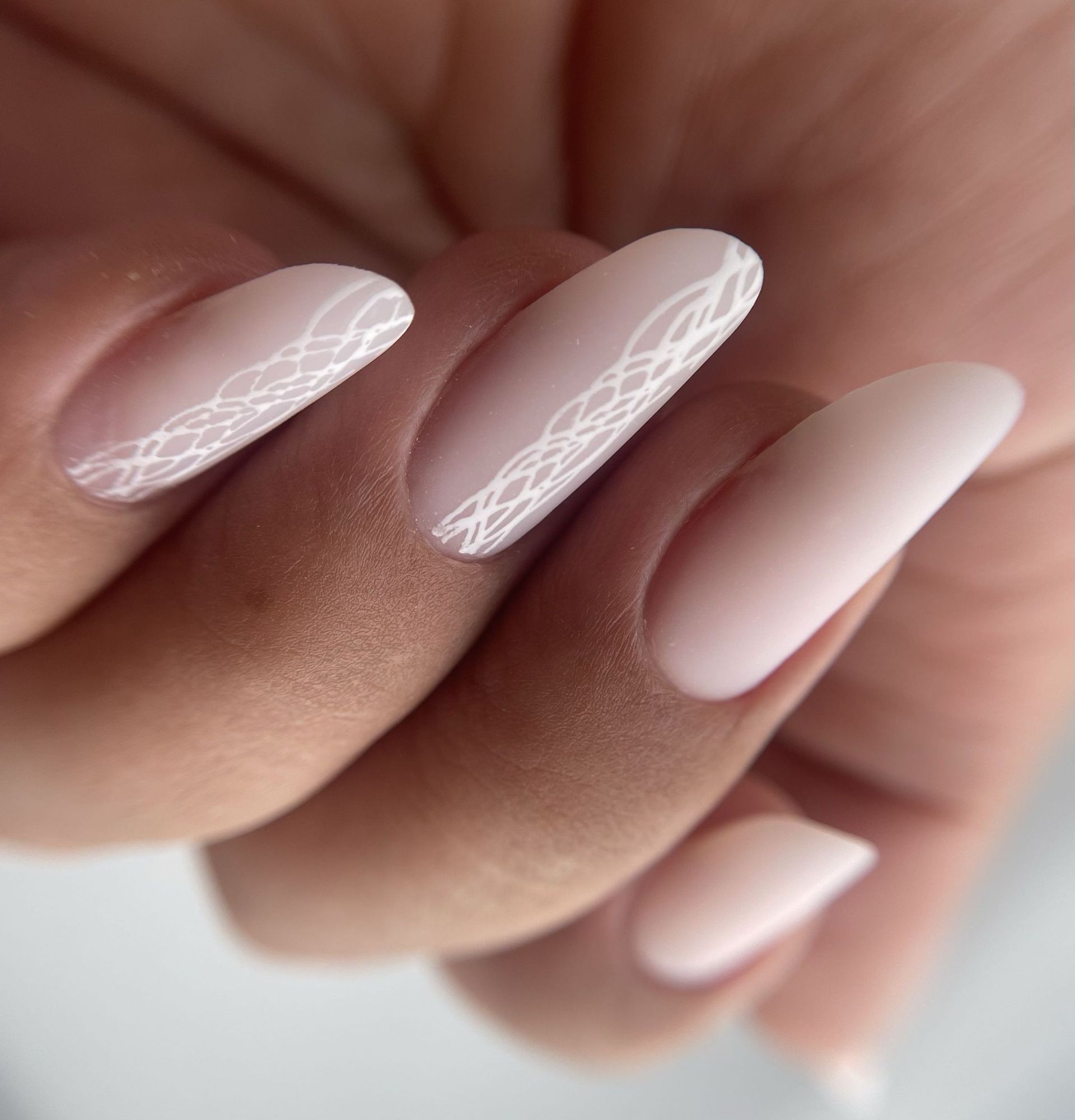 Primer plano de uñas con forma de almendra, con una base suave de color beige mate y delicados detalles de líneas blancas