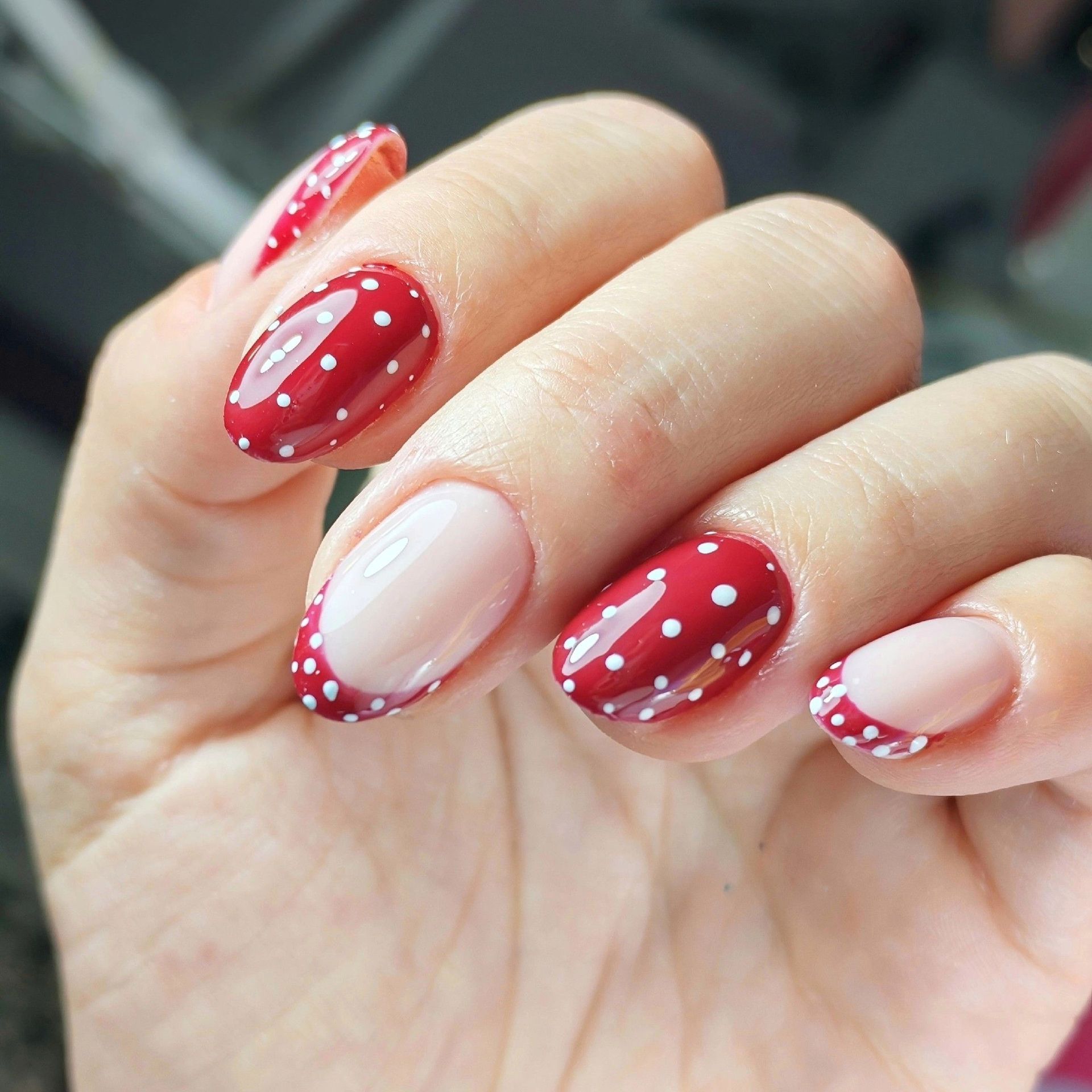 Primer plano de una mano con uñas que alternan entre rojo con lunares blancos y manicura francesa