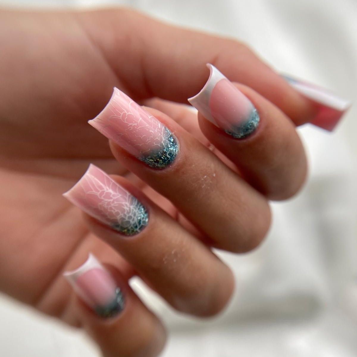 Primer plano de una mano con uñas cuadradas, base rosa, puntas blancas y purpurina turquesa en las cutículas.