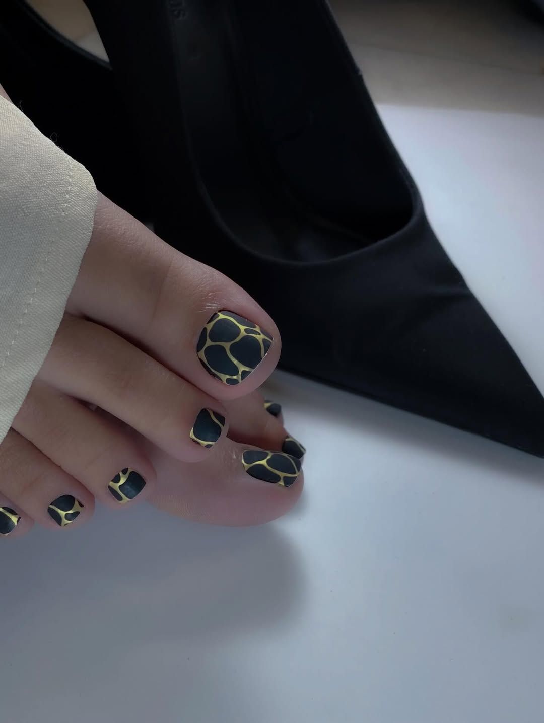 Primer plano de una pedicura con un estampado de jirafa en negro y dorado en las uñas