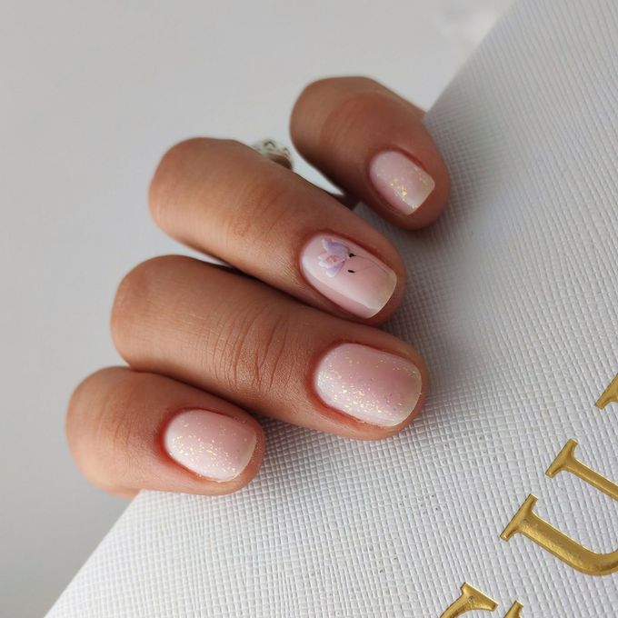 Primer plano de una mano con uñas cortas, brillantes y de color rosa claro