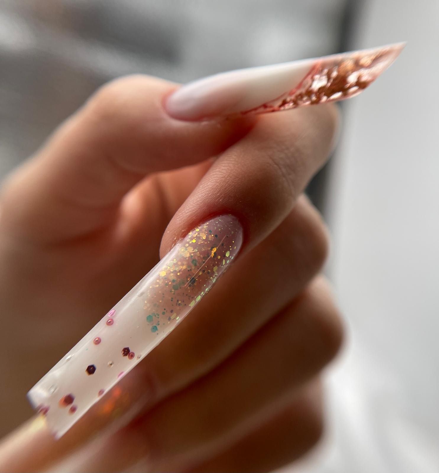 Uñas acrílicas de forma cuadrada con detalles en lámina de oro rosa, pequeñas partículas de purpurina de colores 