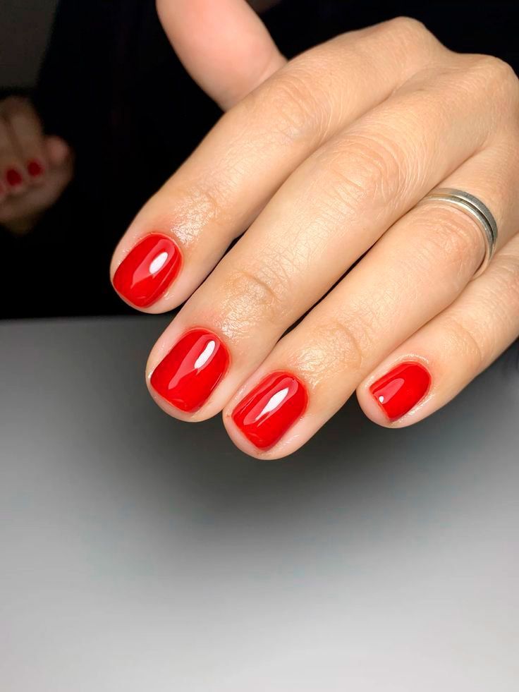 Mano con uñas rojas brillantes y bien cuidadas, y un anillo de plata, descansando sobre una superficie gris.