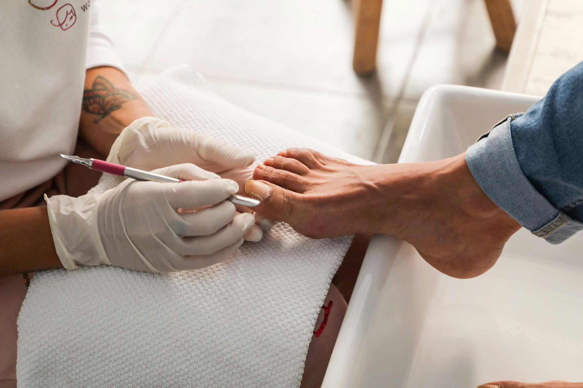Un técnico con guantes utiliza una herramienta para limpiar las uñas de los pies de una persona durante una pedicura 