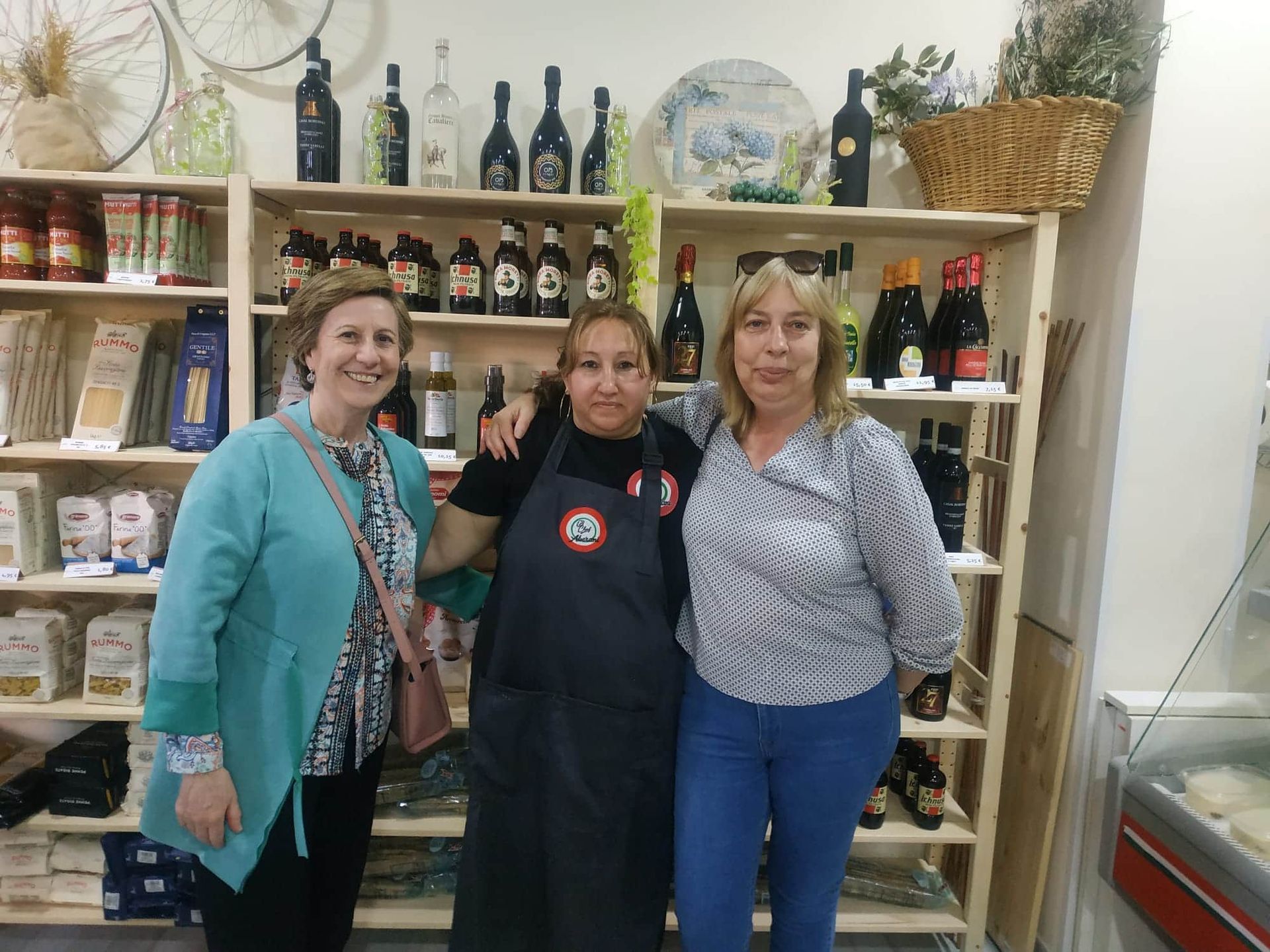 Tres mujeres posan para una foto frente a un estante con botellas.