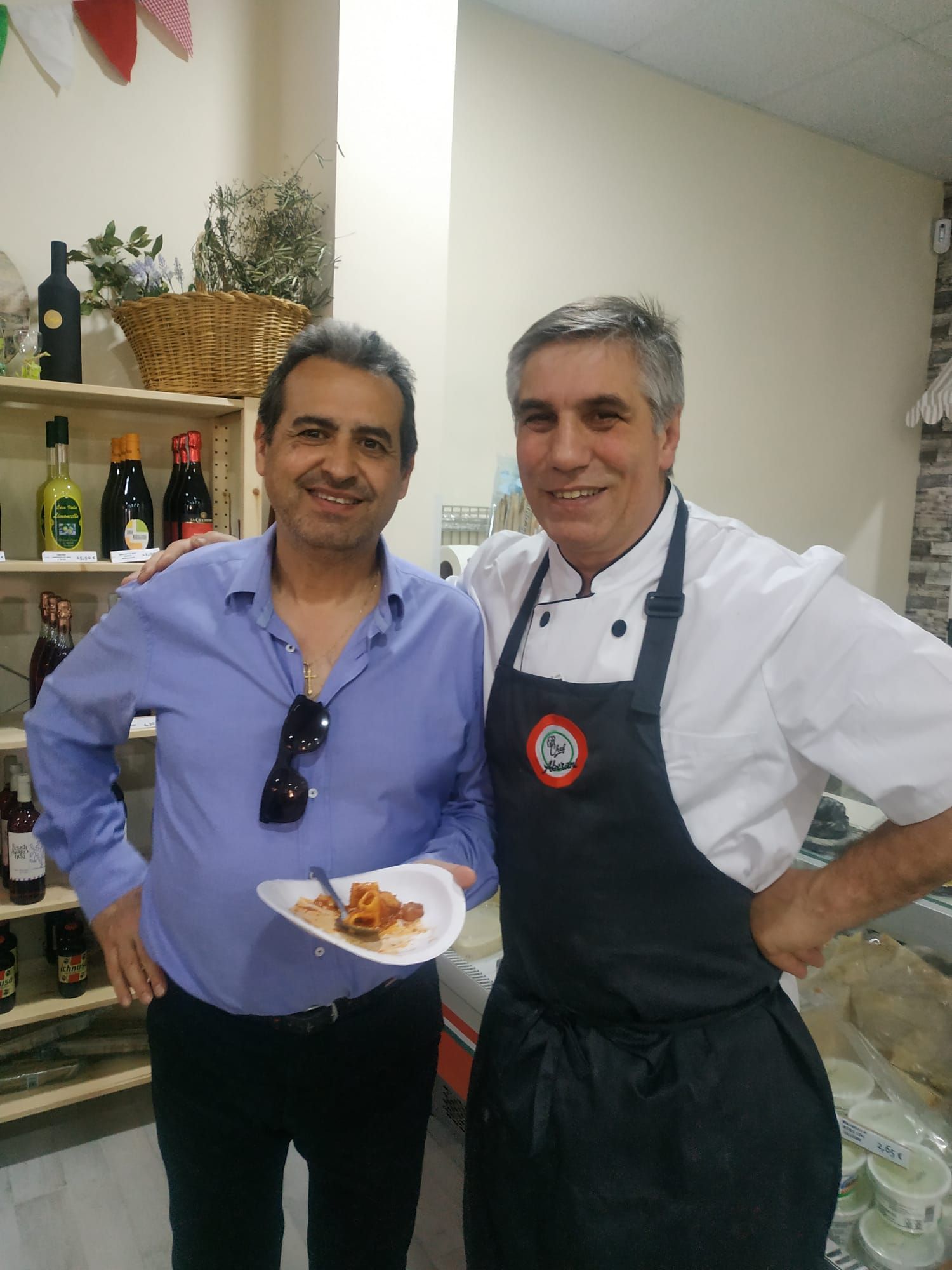 Dos hombres posando para una foto, uno de ellos sosteniendo un plato de comida.
