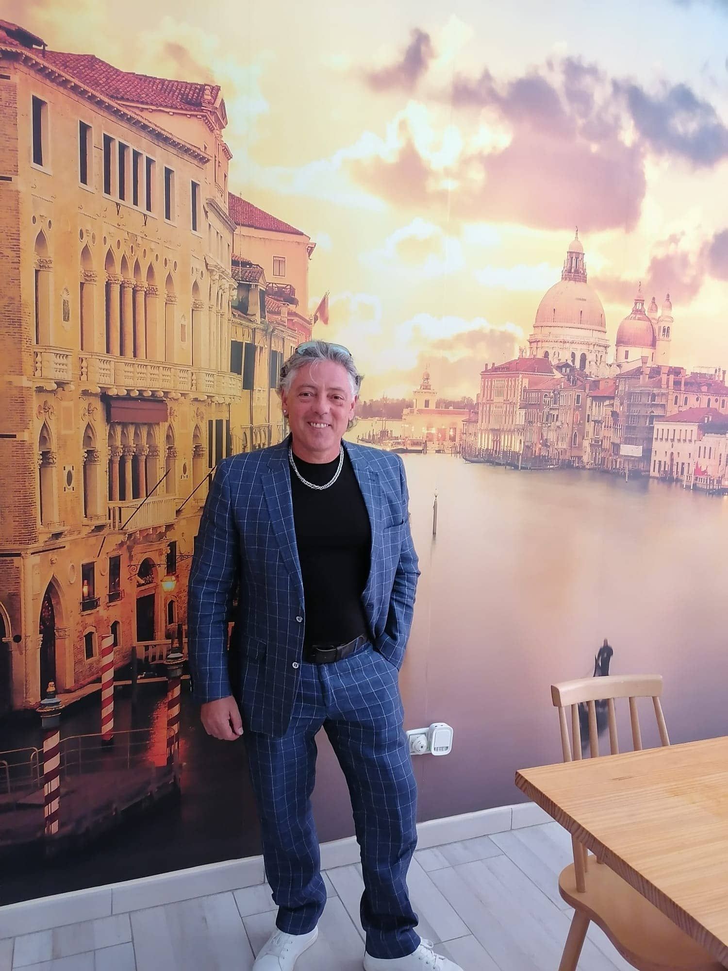Un hombre con traje se encuentra frente a una imagen de Venecia.