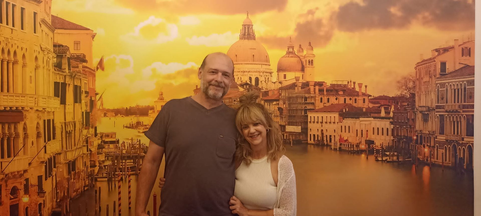 Un hombre y una mujer posan para una foto delante de un cuadro de Venecia.