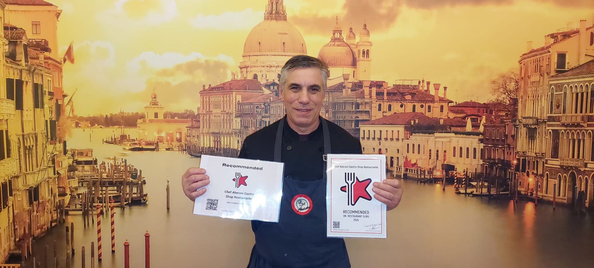 Un hombre con delantal sostiene dos papeles delante de una imagen de Venecia.