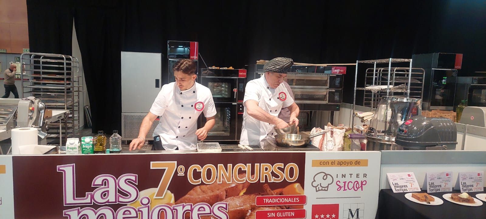 Dos hombres están preparando comida frente a un cartel que dice las 7 mejores del concurso.