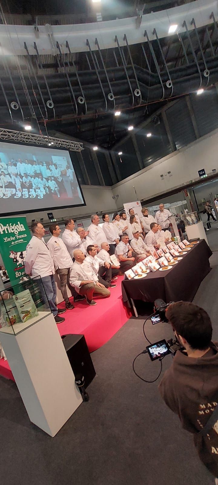 Un grupo de personas están de pie alrededor de una mesa en una habitación grande.