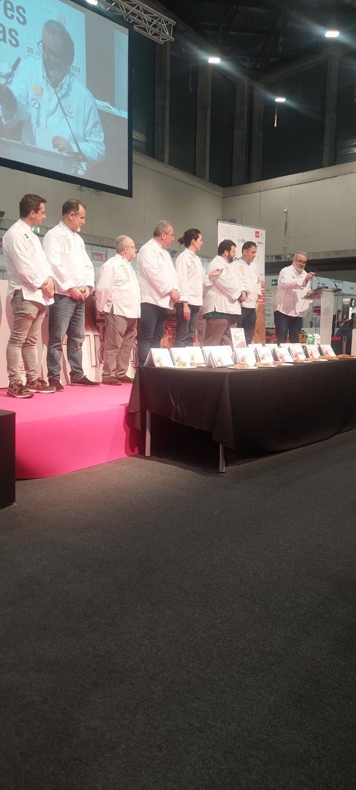 Un grupo de personas está de pie en un escenario frente a una pantalla grande.