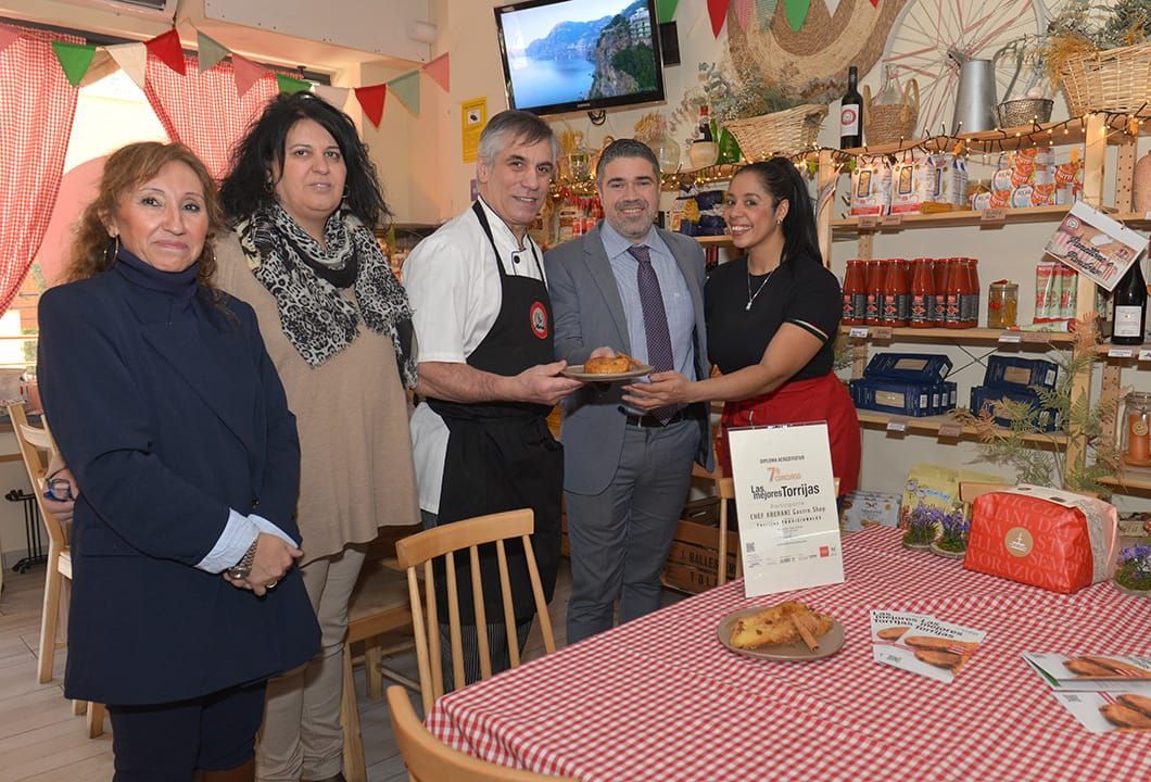 Un grupo de personas de pie alrededor de una mesa con un mantel a cuadros rojos y blancos.