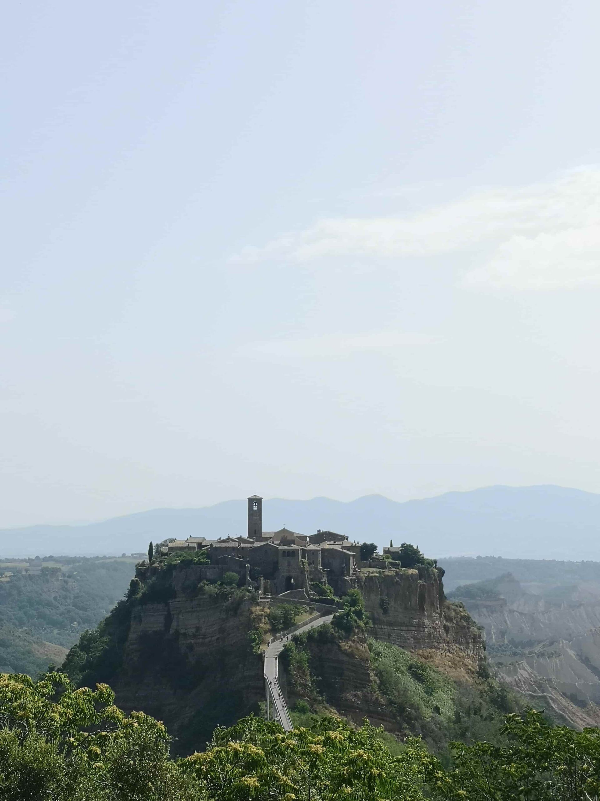 Un pequeño pueblo en la cima de una colina con montañas al fondo.