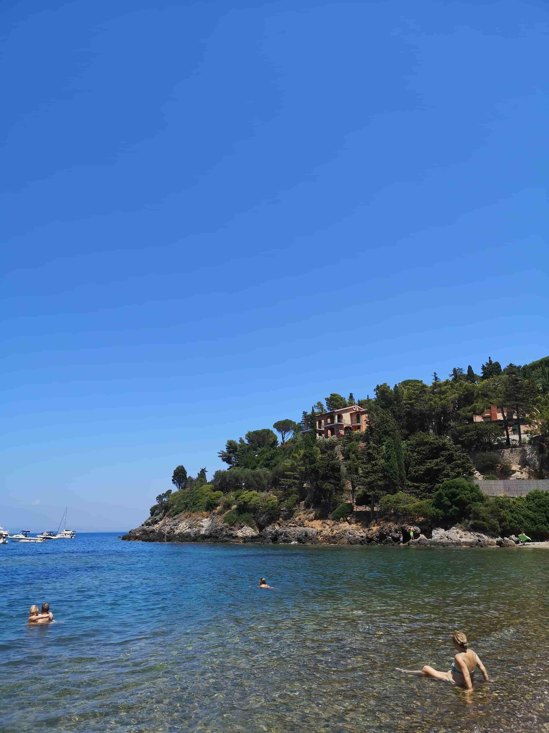 Personas nadando en un cuerpo de agua con una casa al fondo.