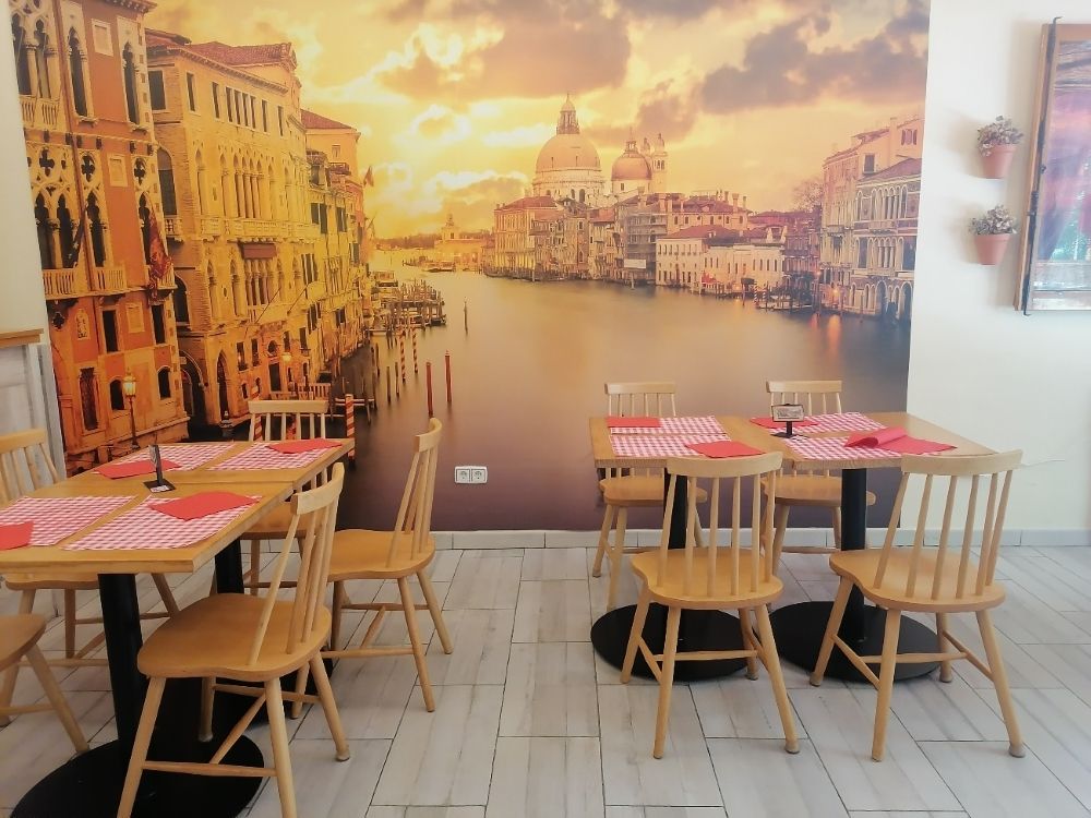 Mesas y sillas en un restaurante con una imagen de Venecia en la pared.