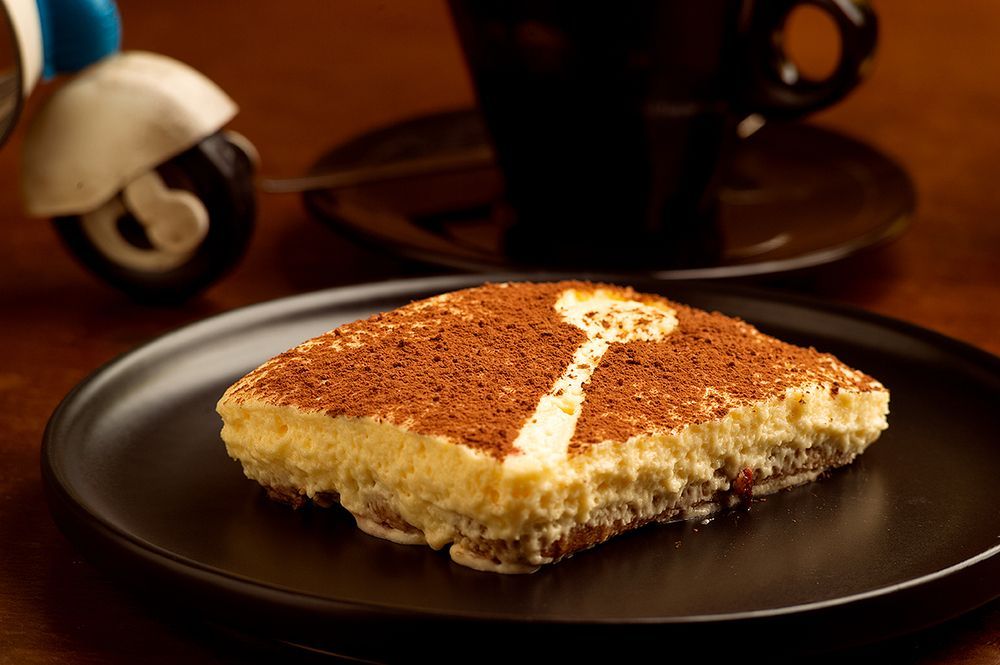 Un trozo de pastel en un plato negro con la letra t en él.