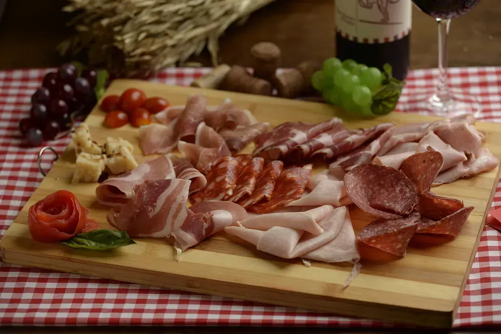 Una tabla de cortar de madera con una variedad de carnes y verduras sobre ella.