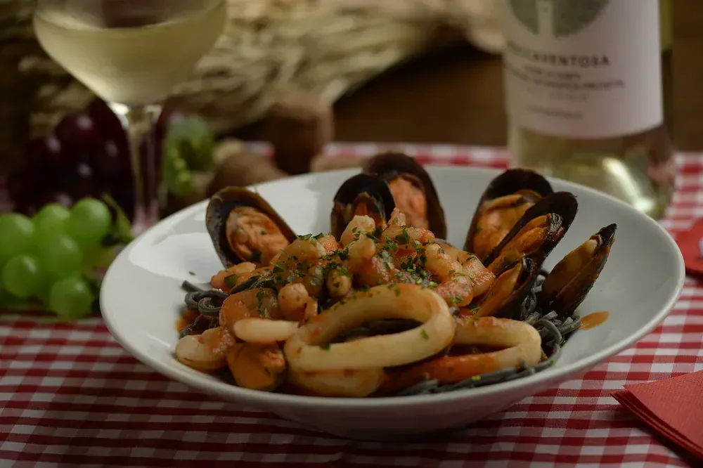 Un plato de mariscos con una botella de vino al fondo.