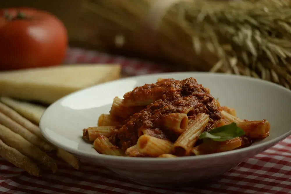 Un plato de pasta con salsa y albahaca sobre un mantel a cuadros.