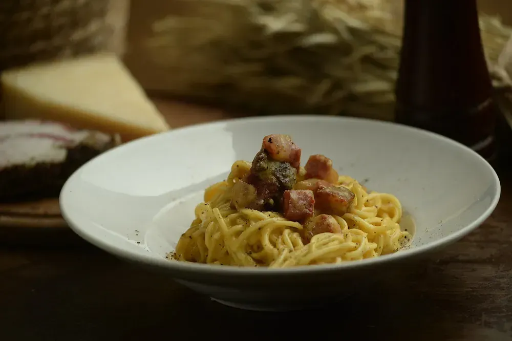 Un plato blanco cubierto con espaguetis y tocino sobre una mesa.