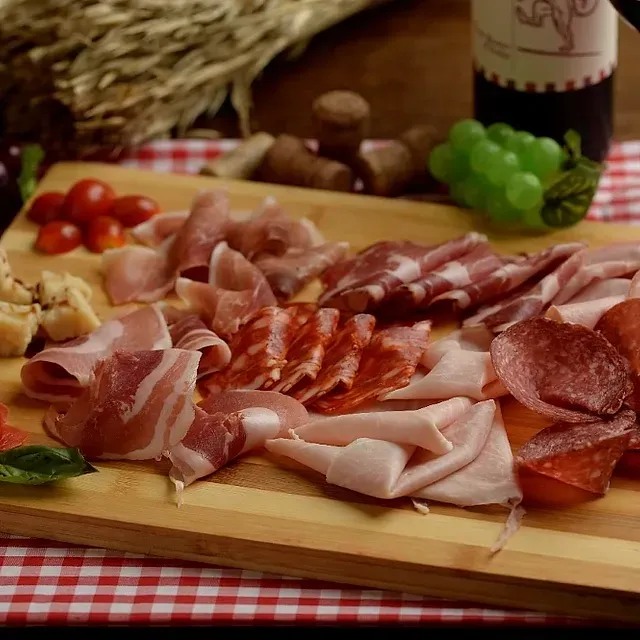 Una tabla de cortar de madera cubierta con una variedad de carnes y verduras.