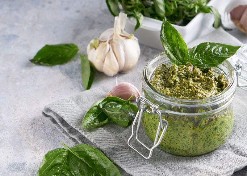 Un tarro de salsa pesto con albahaca y ajo sobre una mesa.