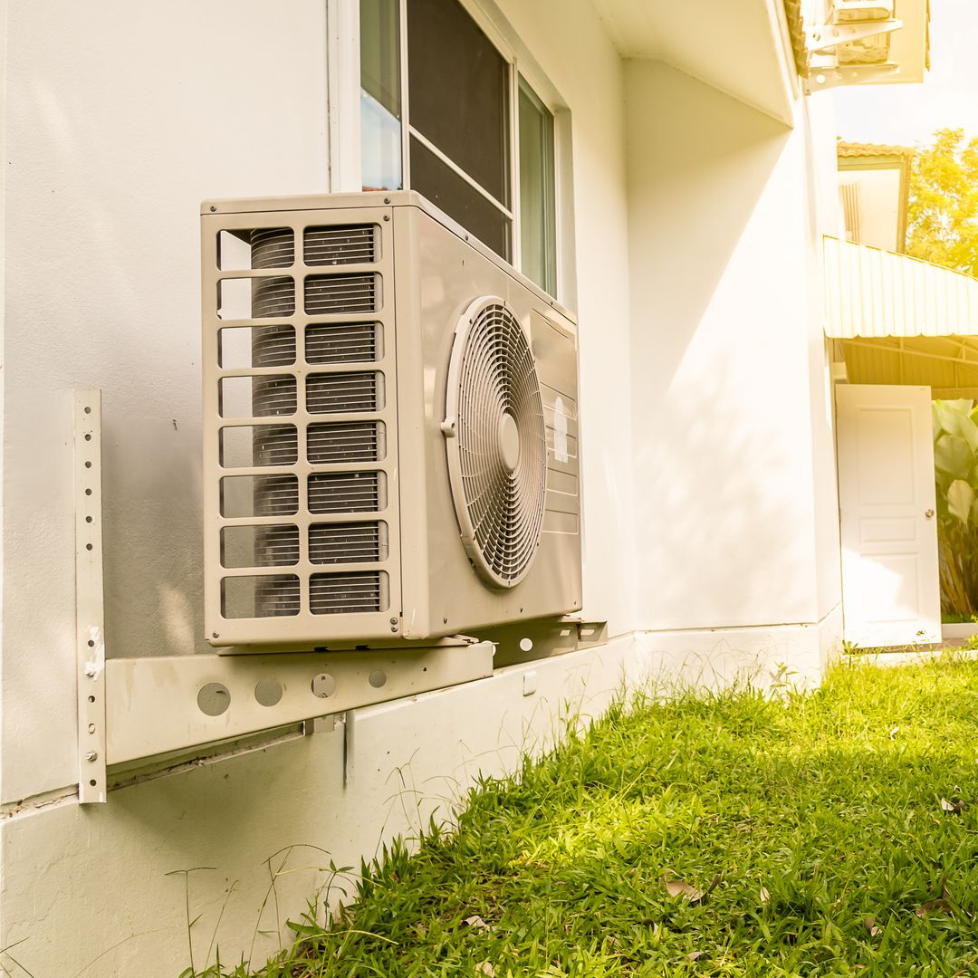 Unité de climatisation extérieure installée sur un bâtiment à côté d'une pelouse.