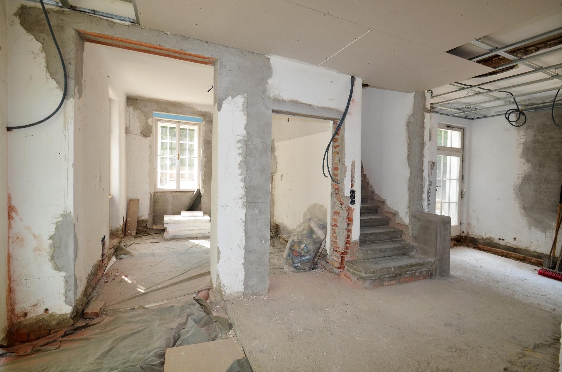 Renovierter Innenraum mit unfertigen Wänden, freiliegenden Kabeln und einer Treppe, die nach oben führt.