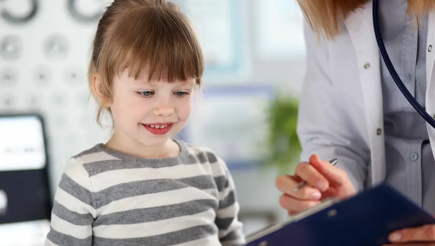 Ein kleines Mädchen schaut auf ein Klemmbrett mit einem Arzt.