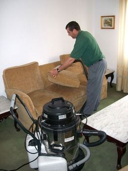 Un hombre está limpiando un sofá con una aspiradora.