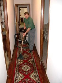Un hombre está aspirando una alfombra roja en un pasillo.